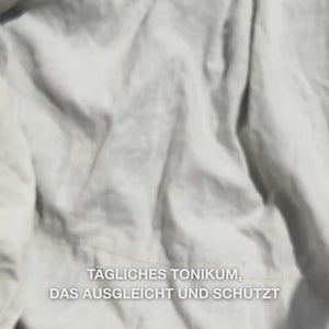 Nahaufnahme einer Hand, die einige Tropfen des klaren, wässrigen Face Tonic mit Teebaumöl auf ein Wattepad gibt und es dann sanft über die gereinigte Gesichtshaut streicht: die leichte, erfrischende Flüssigkeit beruhigt, reinigt tief, spendet Feuchtigkeit und hinterlässt die Haut erfrischt und optimal vorbereitet für eine Creme.