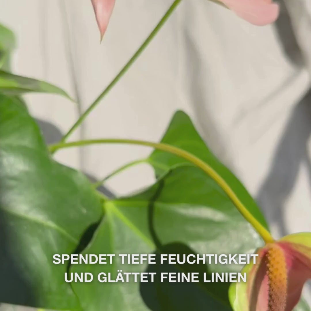 Nahaufnahme einer Hand, die einige Tropfen eines seidigen, klaren Gesicht‑Serums aus einem Glas-Tropfer auf die Fingerspitzen gibt und es sanft in leicht feuchte Haut einmassiert – die leichte, schnell einziehende Textur spendet sofort Feuchtigkeit, glättet feine Linien und beruhigt die Haut mit 2 % Hyaluronsäure, Vitamin B5 und Teebaumöl 