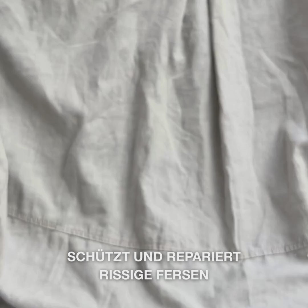 Nahaufnahme einer Hand, die die reichhaltige, cremige Heel Repair-Textur in die Handfläche nimmt und sanft in trockene, rissige Fersenhaut einmassiert: Die dicke Konsistenz wird sichtbar aufgenommen, macht raue Stellen weich und geschmeidig, während 25 % Harnstoff, Sheabutter und Teebaumöl beruhigend sowie schützend wirken.