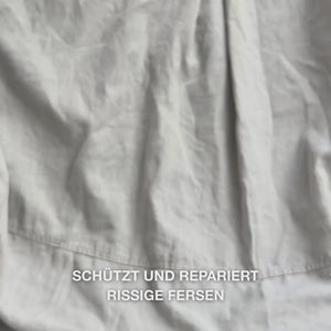 Nahaufnahme einer Hand, die die reichhaltige, cremige Heel Repair-Textur in die Handfläche nimmt und sanft in trockene, rissige Fersenhaut einmassiert: Die dicke Konsistenz wird sichtbar aufgenommen, macht raue Stellen weich und geschmeidig, während 25 % Harnstoff, Sheabutter und Teebaumöl beruhigend sowie schützend wirken.